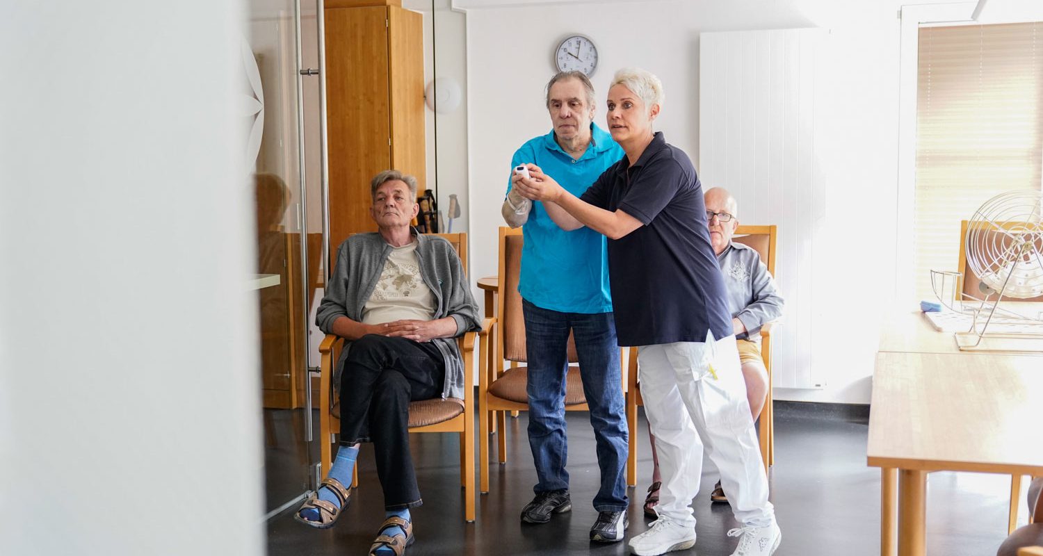 alwo-pflegezentrum_aktivitaeten_bowling Bewohner spielen an Bowling an einer Spielekonsole während eine Pflegekraft hilft