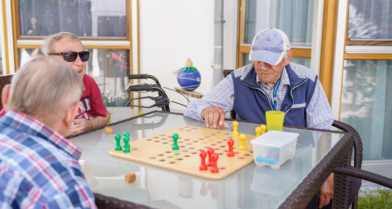 alwo_artelshofen-tageszentrum_1500x1000px Drei Bewohner spielen draußen ein Brettspiel